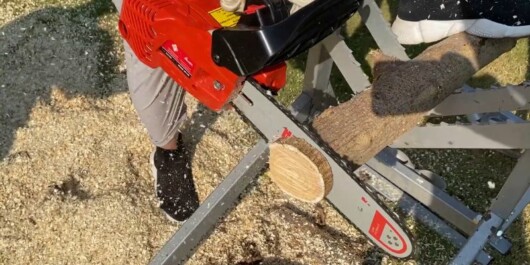 person using troy-bilt chainsaw to cut logs into pieces